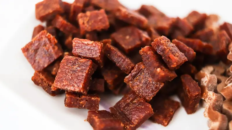 A pile of cubed, spicy beef jerky on a white surface.